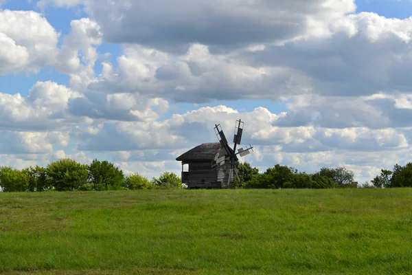 Alte hölzerne Windmühle im grünen Feld über strahlend blauem Himmel und Wolken — Stockfoto