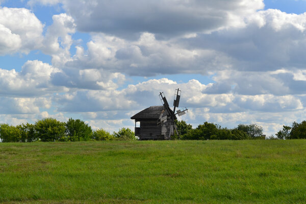 Old wooden windmill in green field over bright blue sky and clouds
