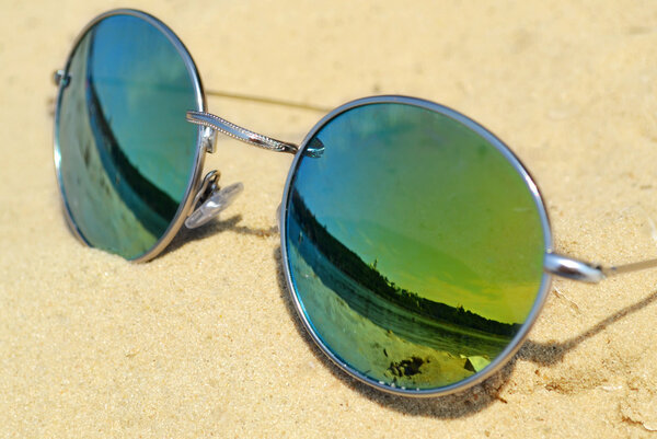 Mirrored sunglasses on sand with a reflection of the beach
