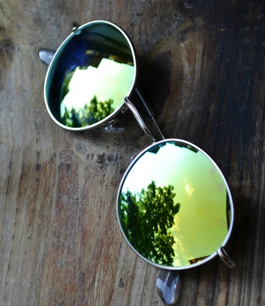 Lunettes de soleil couchées sur une table en bois avec un reflet d'arbres — Photo