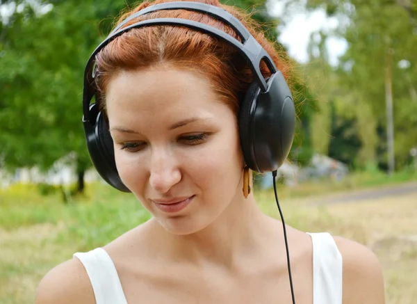 Mujer pelirroja hermosa en grandes auriculares escuchando la música con sonrisa feliz — Foto de Stock