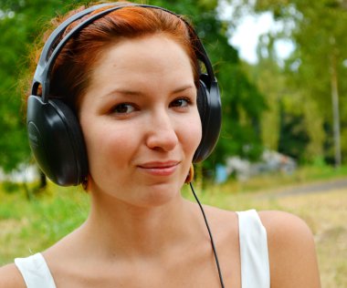 büyük Kulaklığımda mutlu bir gülümseme ile müzik dinlemek güzel kızıl saçlı kadın