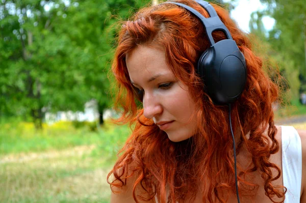 Vakker, rødhåret kvinne i store hodetelefoner som hører på musikk – stockfoto