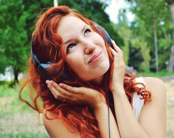 Mulher ruiva bonita em grandes fones de ouvido ouvindo a música com sorriso feliz — Fotografia de Stock