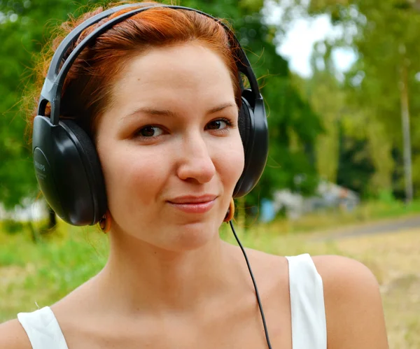 Frumoasă femeie roșcată în căști mari ascultând muzica cu zâmbet fericit — Fotografie, imagine de stoc
