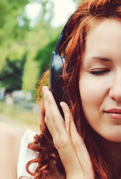 Mujer pelirroja hermosa en grandes auriculares escuchando la música con los ojos cerrados — Foto de Stock