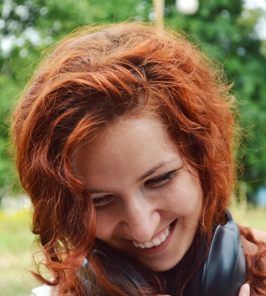 Hermosa joven pelirroja sonriendo felizmente con grandes auriculares en su cuello — Foto de Stock