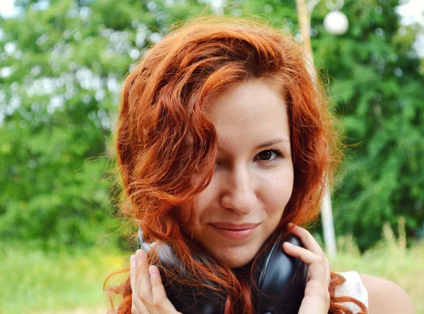 Wanita cantik berambut merah tersenyum bahagia dengan headphone besar di lehernya — Stok Foto