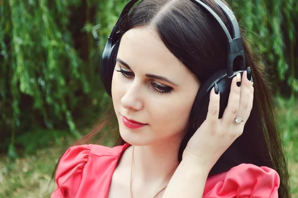 Hermosa mujer morena en grandes auriculares escuchando la música con sonrisa feliz — Foto de Stock