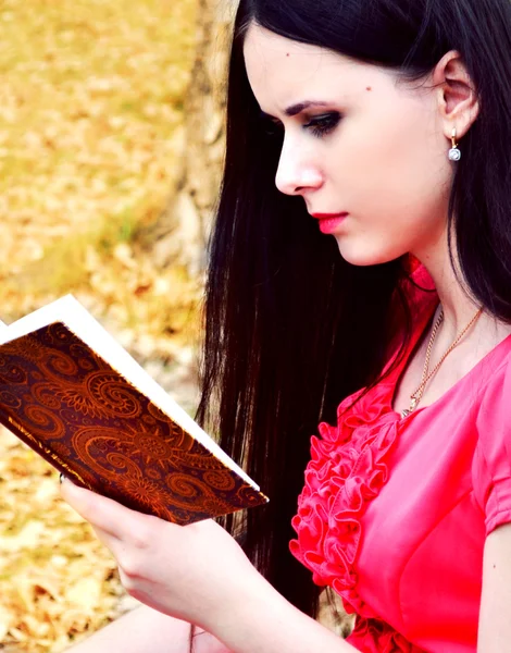 Beautiful brunette woman with long hair reading against autumn nature — Stock Photo, Image