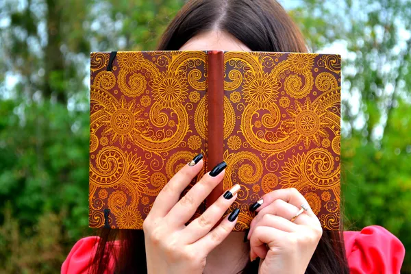 Shy brunette woman hiding behind a notebook — Stock Photo, Image