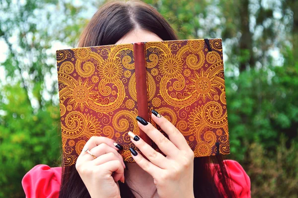 Shy brunette woman hiding behind a notebook — Stock Photo, Image