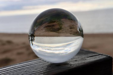 Baltık Denizi üzerinde güneş ışığı bulutları, durgun mavi deniz, beyaz bulutlar, ve kristal bir kürenin içinden görünen bazı dal siluetleri