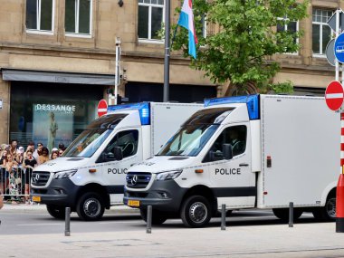 White police vans with strobe lights flashing drive on National day parade. Luxembourg, Luxembourg - June 23, 2022. Selective focus