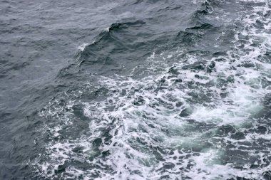 Gri mavi deniz suyunda beyaz köpüklü kıç dalgaları, gemide çekilmiş bir fotoğraf. Seçici odak