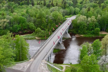 Letonya 'nın Sigulda kentindeki Gauja Nehri üzerinde birçok Letonya bayraklarıyla süslenmiş bir köprünün havadan çekilmiş fotoğrafı. Boşalt