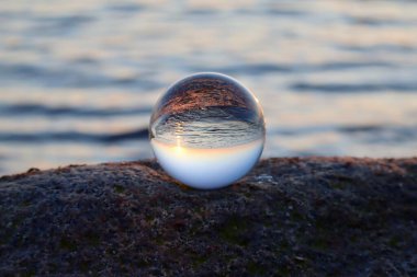 Crystal ball on rocky beach on a granite boulder, sunset reflecting in the sea, background blurred