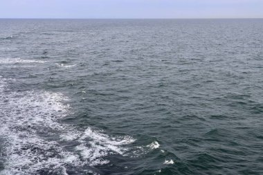 Gri mavi deniz suyunda beyaz köpüklü kıç dalgaları, gemide çekilmiş bir fotoğraf. Seçici odak