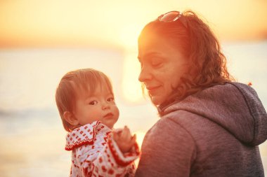 Kışın güzel gün batımı. Kamp yapmak. Ebeveynler ve çocuklar sahilde okyanusun kenarında oturuyorlar. Turizm. Anne ve kızı kış denizinin kıyısındaki günbatımına hayran..