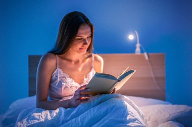 Güzel bir kadın yatmadan önce yatak odasında loş ışıklı bir kitap okur. Rahatlama. Edebiyat. Kendi kendini geliştirme
