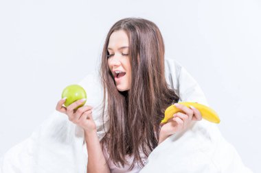 Kız yatağa oturur, bir battaniyeye sarınır, bir muz tutar ve bir elmaya bakar. Esmer, meyveyle kahvaltı yapıyor..