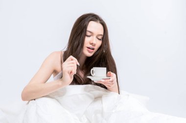 Beyaz yatak odası. Esmer, elinde sıcak bir içecekle bir fincan tutuyor. Bir kadın yatakta oturuyor, aromatik kahve içiyor. Lezzetli bir kahvaltı. Günaydın..