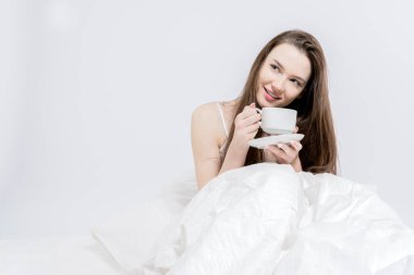 Beyaz yatak odası. İyi sabahlar. Esmer, elinde sıcak bir içecekle bir fincan tutuyor. Bir kadın yatakta oturuyor, aromatik kahve içiyor. Lezzetli kahvaltı..