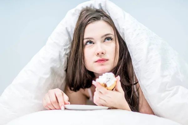 Μια Χαριτωμένη Γυναίκα Τρώει Ένα Κεκάκι Ξαπλωμένη Στο Κρεβάτι Κάτω — Φωτογραφία Αρχείου