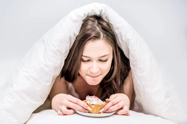 Een Leuke Vrouw Kijkt Met Eetlust Naar Een Cupcake Liggend Stockfoto