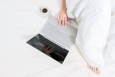 Laptop beyaz bir yatakta bir fincan kahve ve bir kızın yanında yatıyor. İyi sabahlar. Evden çalış..