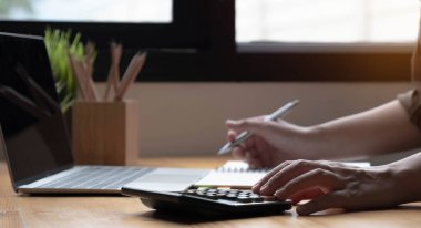 İş verilerini, muhasebe belgelerini ve ofisteki dizüstü bilgisayarları, iş konseptini hesaplamak için hesap makinesi üzerinde çalışan kadın ya da muhasebecinin elini kapat.