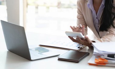 Hesap makinesi ve yazı kullanan bir iş kadını, hesap makinesiyle not alır. Ofiste çalışan bilgisayarlı ve belgeli bir kadın.