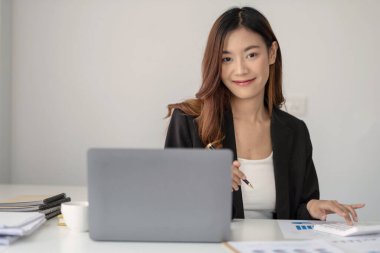 Ofiste çalışan yakışıklı Asyalı kadın dizüstü bilgisayar kullanıyor. Kameraya bakıyor.