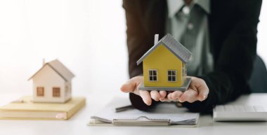 Miniature house in the hands of an Asian woman real estate agent home loan working at the office. Looking at the camera