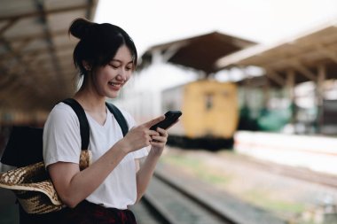 Woman waiting on station platform on background light train using smart phone. Tourist texting message and plan route of stop railway, railroad transport, booked. Enjoying travel concep