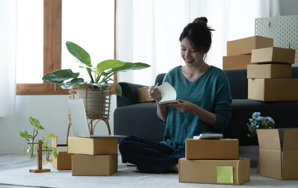 Asian women write note of orders of goods with a smiling face in concept of sme, e-commerce busines