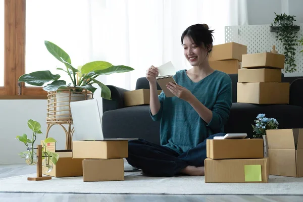 Asian women write note of orders of goods with a smiling face in concept of sme, e-commerce busines