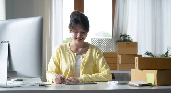 Portrait business Asian woman smile and use tablet checking information on parcel shipping box before send to customer. Entrepreneur small business working at home. SME business online marketing