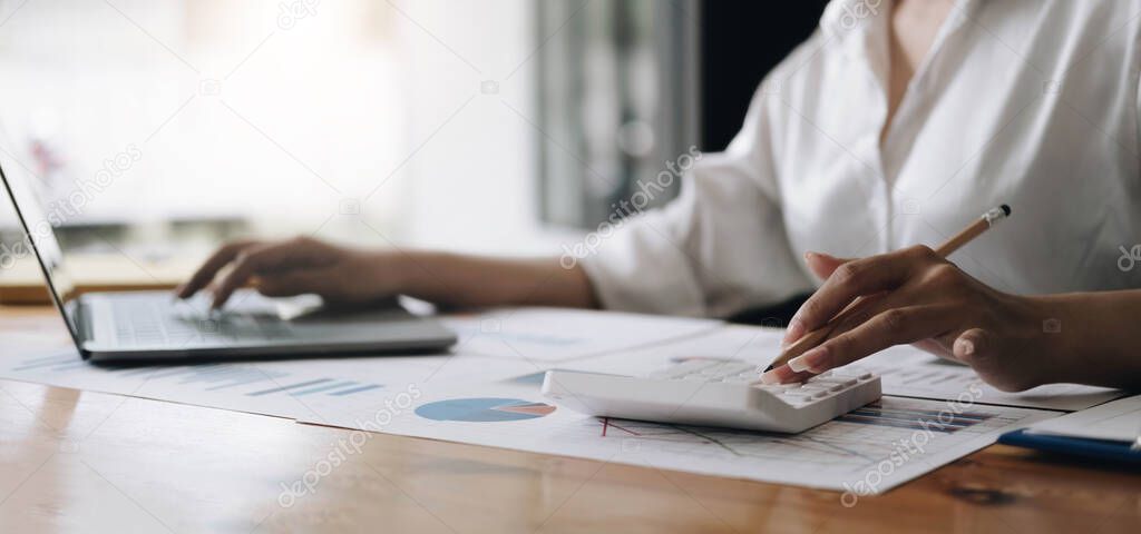 Close up Business woman using calculator and laptop for do math finance on wooden desk in office and business working background, tax, accounting, statistics and analytic research concep