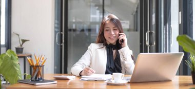 Güzel, genç Asyalı bir kadın kafeteryada akıllı telefon kullanıyor. Kafedeki masada oturan mutlu genç iş kadını, en üst düzey bilgisayarla.