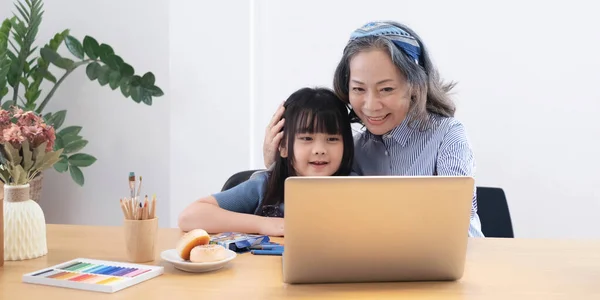 Asian grandmather teach granddaughter drawing and doing homework at home.