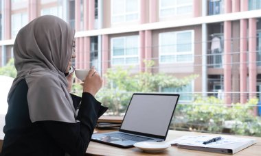 mutlu güzel Müslüman kadın işçi ofisinde oturan ve mobil cep telefonu online haber rahatlatıcı ile ilgilenen kullanarak sıcak kahve kupa holding