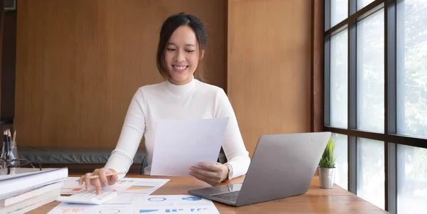 Portrait of Young Asian woman hand freelancer is working her job on computer tablet in modern office. Doing accounting analysis report real estate investment data, Financial and tax systems concept