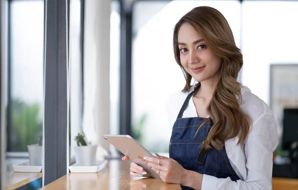 Startup successful small business owner sme beauty girl stand with tablet smartphone in coffee shop restaurant. Portrait of asian tan woman barista cafe owner. SME entrepreneur seller business concep