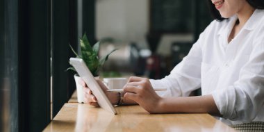 Güzel genç Asyalı kadın ya da kız üniversite öğrencisi kahve dükkanında oturup portatif tablet dokunmatik ped kullanıyor.