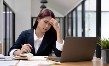Genç Asyalı kadın migren ağrısı çekiyor. Ofiste dizüstü bilgisayarla çalışırken çok çalışan iş kadını finansörü.