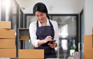 Portrait, entrepreneur, young Asian woman, freelance business, sme business, online shopping, working on laptop computer with parcel box on home office table, online business and delivery concept