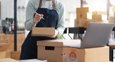 Startup Entrepreneurship Small Business SME Freelance Young lady working at home with boxes and laptop online Marketing Packaging SME Shipping Ecommerce Concept