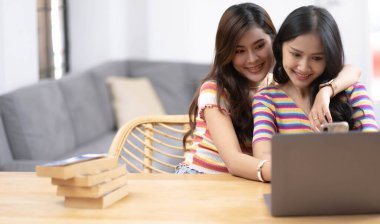 Genç ve güzel Asyalı lezbiyen çift, akıllı telefonları ve dizüstü bilgisayarları kullanarak mutlu bir yaşam tarzı olan LGBT cinselliği kavramı ile evde, gülümseyen yüzüyle birlikte online alışveriş yapıyor.