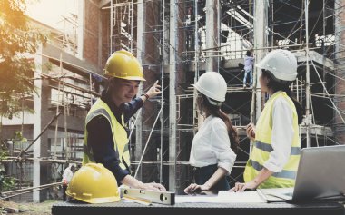 A diverse team of experts are planning on the construction site. Real estate project with civil engineers, architects, business investors and the general staff are discussing the details of the plans